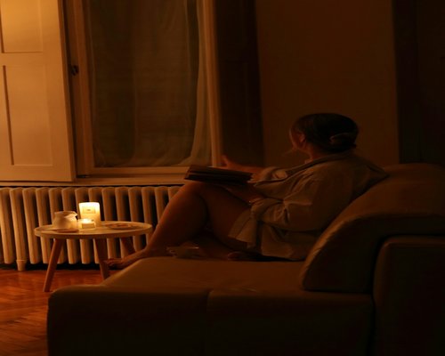 A person sitting in a comfortable armchair, reading a physical book under a soft ambient lamp light in the evening